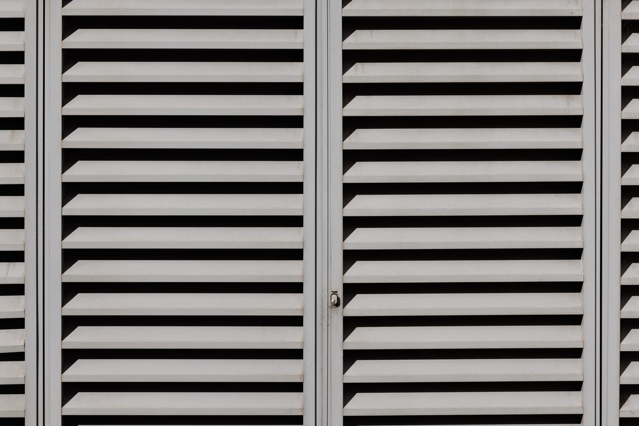 Close-up view of an industrial louvered metal door with horizontal slats and a central locking mechanism, designed for ventilation and security.