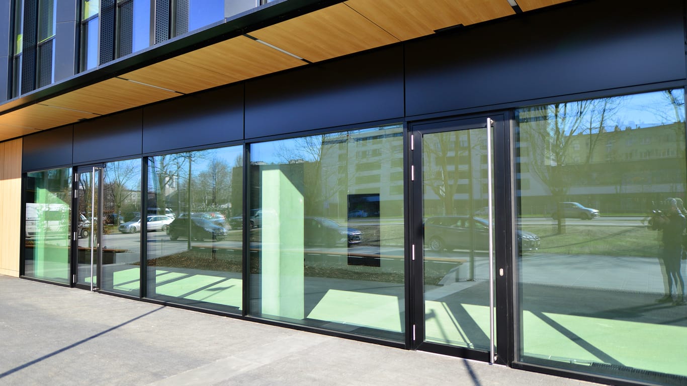 Modern commercial building with black steel-framed glass storefront, ideal for businesses seeking Storefront Glass Repair in Sunny Isles Beach. The structure features large windows, wooden paneling overhead, and reflections of the street and parked cars.