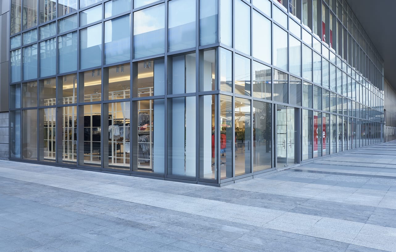 Modern glass storefront of a clothing store with large floor-to-ceiling windows displaying clothing items. The building exterior features a sleek, grid-like design with clean lines.