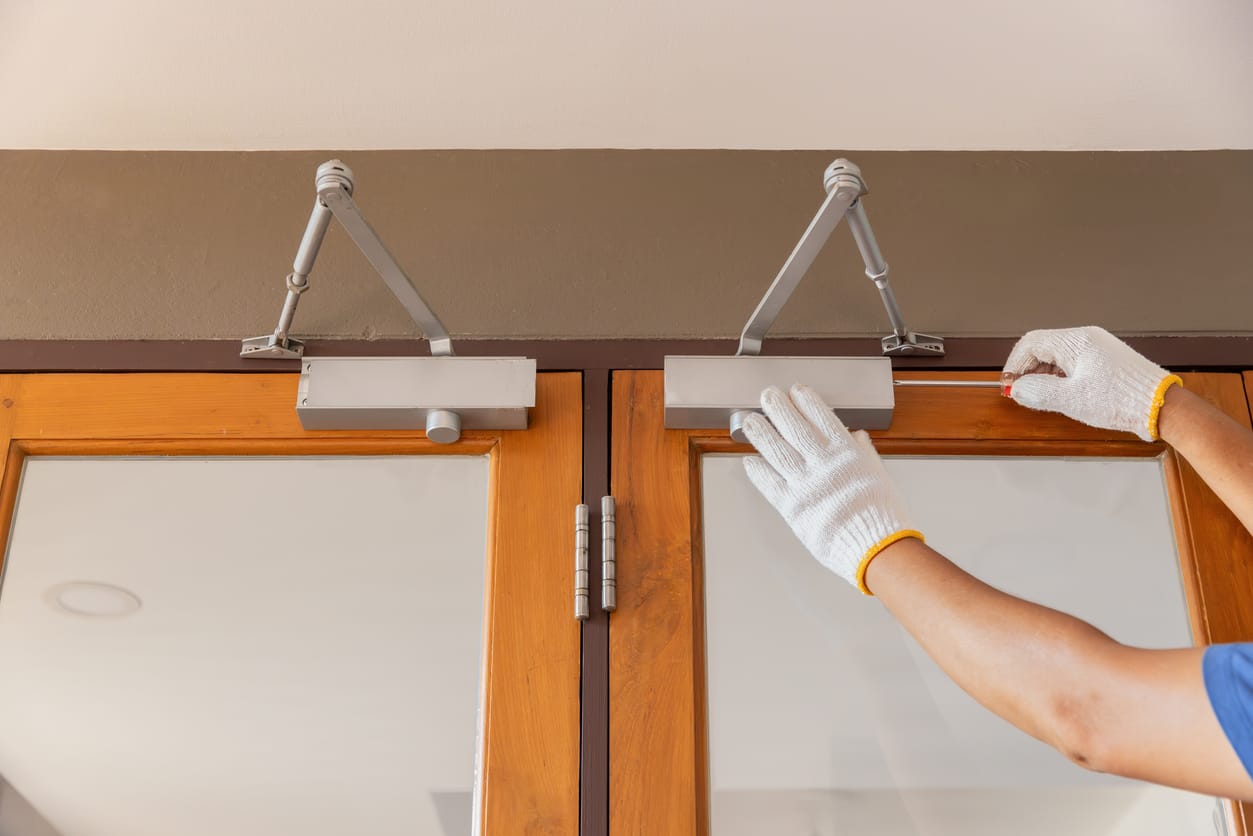 Technician wearing white gloves performing commercial door repair on a wooden door by adjusting the overhead door closer.