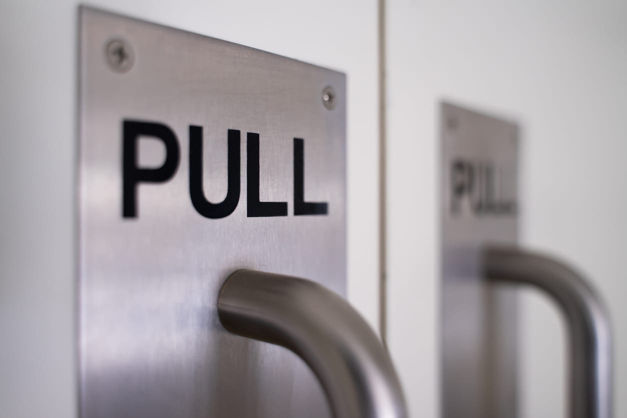 Close-up view of a brushed stainless steel commercial door plate with the word 'PULL' engraved and a curved handle.