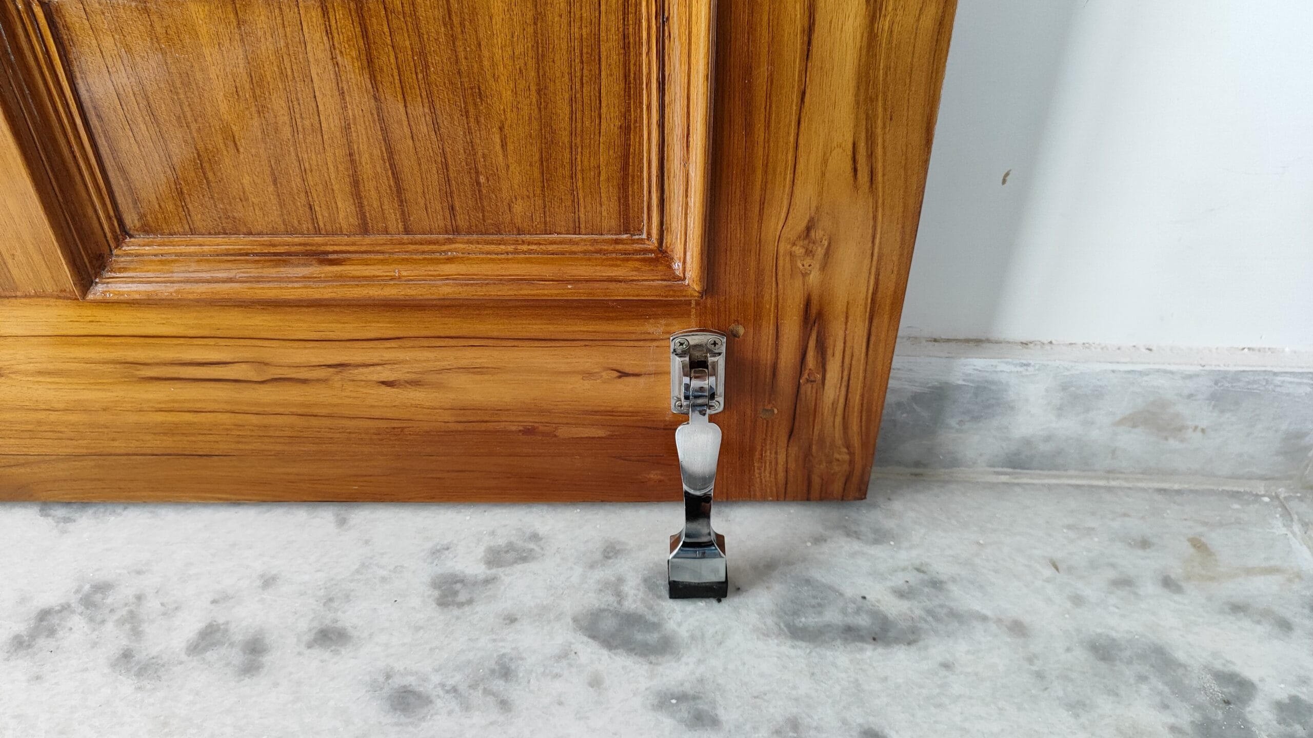 Close-up view of a kick down door stop installed on a wooden door, resting on a polished marble floor, highlighting its practical design and secure mounting.