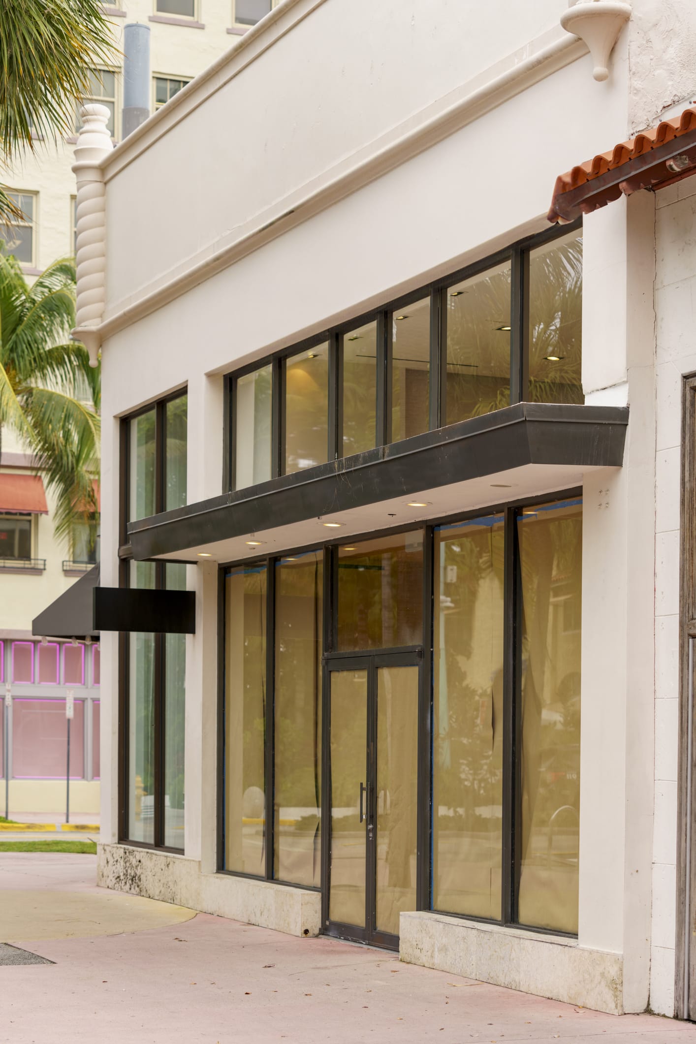 framed glass storefront door with transom above, set in white cement in bright neighborhood.