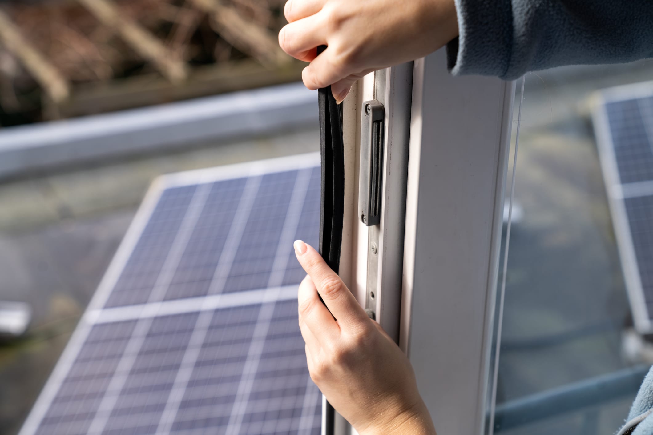 Woman installing weather stripping on a commercial door, with solar panels visible in the background, emphasizing energy efficiency and sustainability.